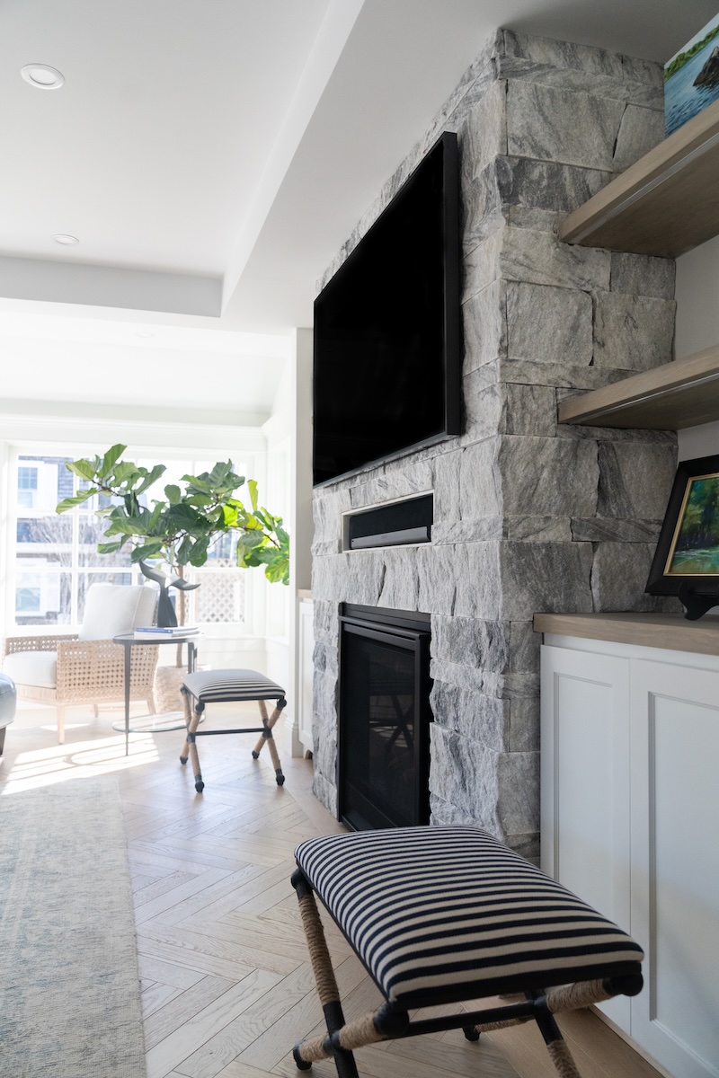 Georgia Marble Pearl Grey marble veneer fireplace in open-plan coastal living room — Berkshire™ split-face thin veneer surround with natural light, herringbone floor and sunroom beyond