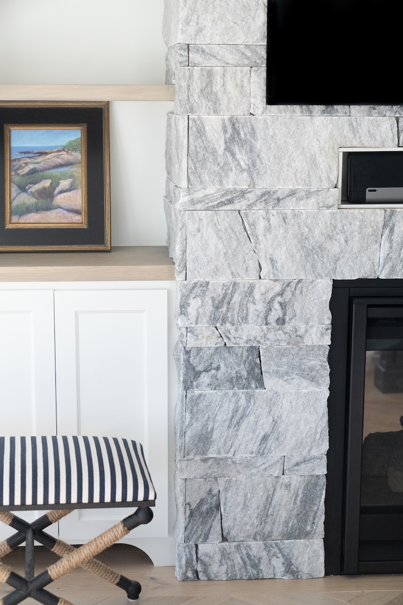 Left column detail of Berkshire™ Georgia Marble Pearl Grey fireplace veneer — full height split-face marble veneer surround with built-in cabinetry and coastal artwork
