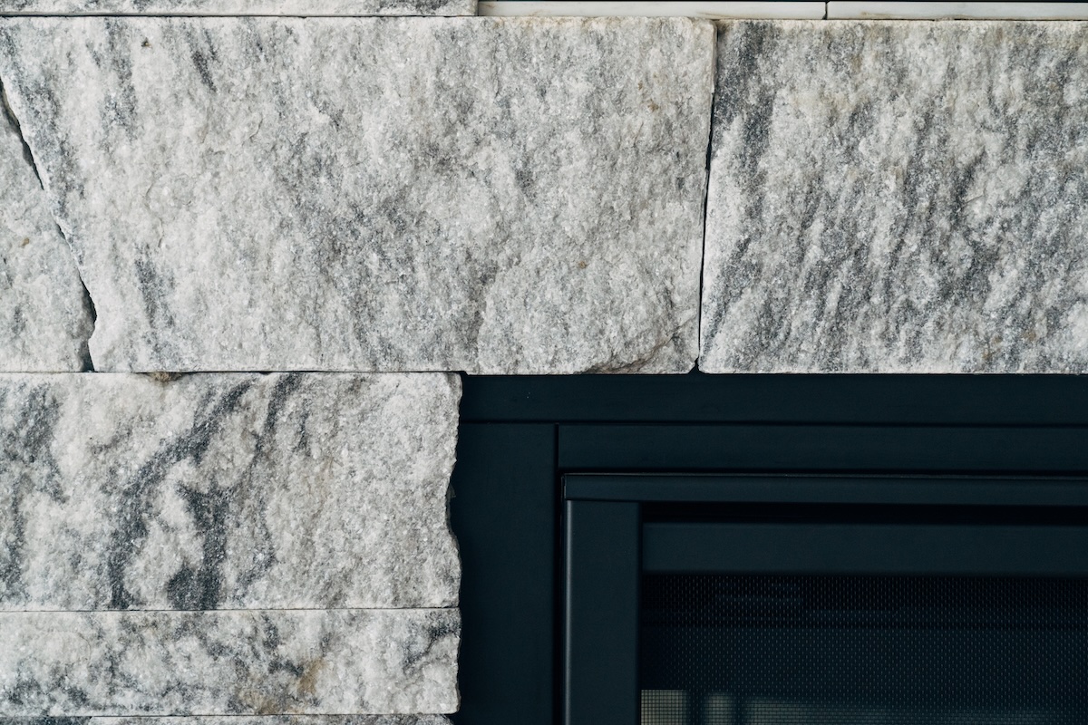 Close-up of Georgia Marble Pearl Grey™ split-face thin veneer at fireplace opening — sawn edge detail meeting black gas firebox frame, Berkshire marble veneer texture