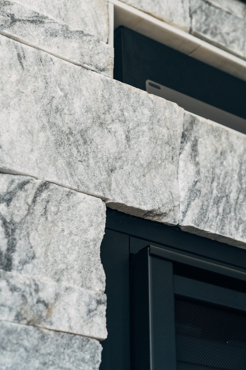 Split-face Georgia Marble Pearl Grey thin veneer corner detail at fireplace opening — Berkshire™ natural marble veneer showing organic edge texture and grey veining
