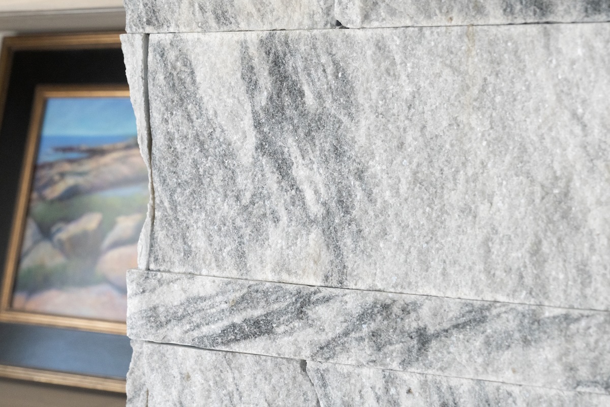 Berkshire™ Georgia Marble Pearl Grey thin veneer fireplace column — sawn edge profile and split-face texture detail with coastal landscape painting in background